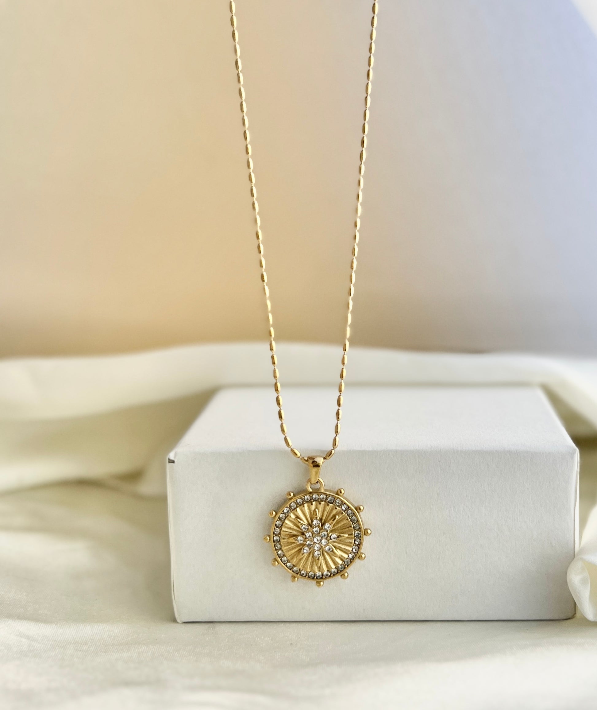 Gold necklace with a circular pendant on a white box