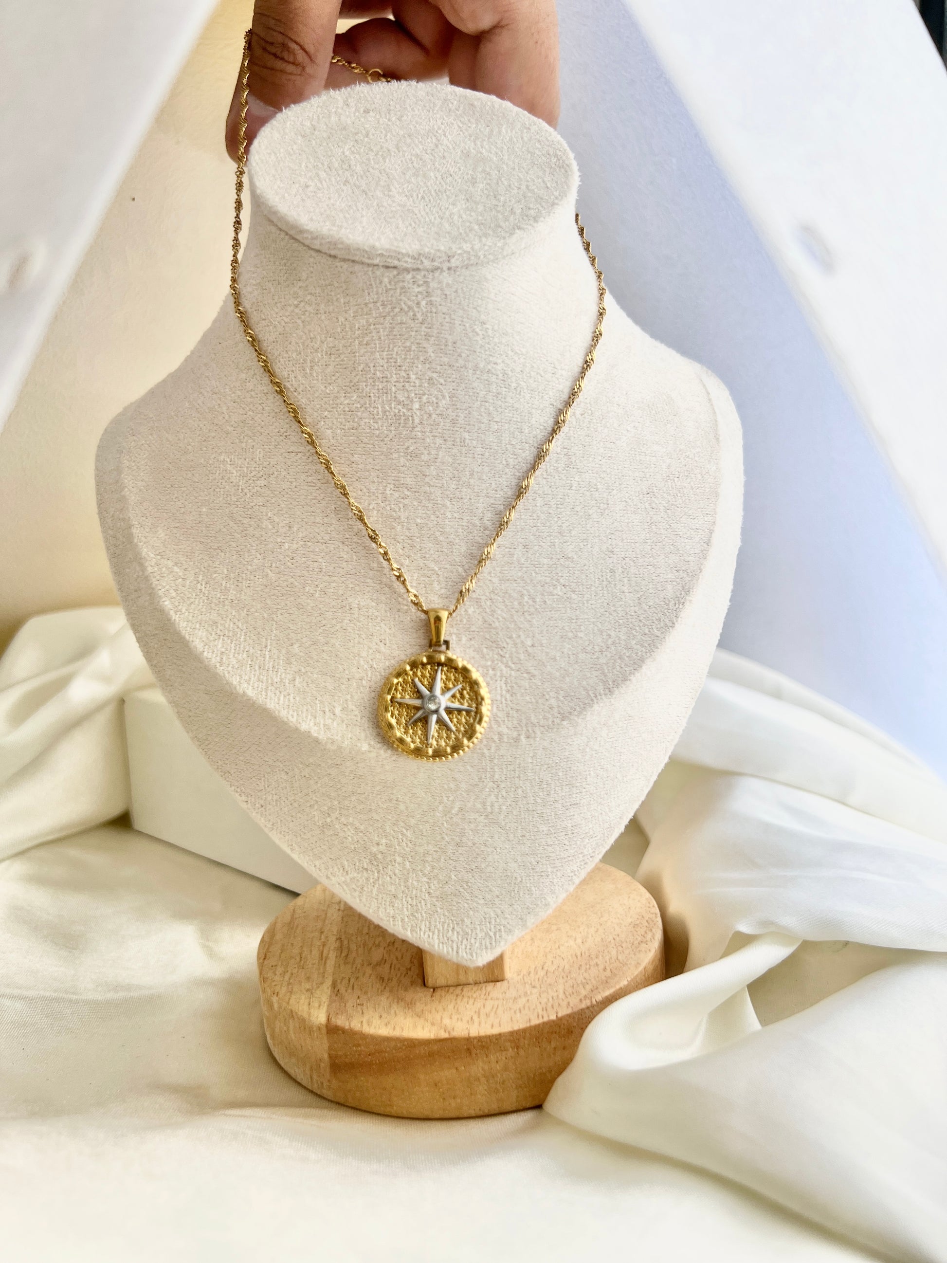 Gold necklace with a star pendant on a white jewelry stand.