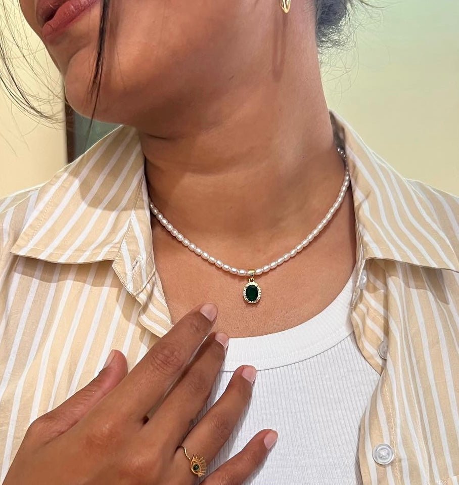 A person wearing a white and yellow striped shirt, with a green emerald necklace and a pearl strand.