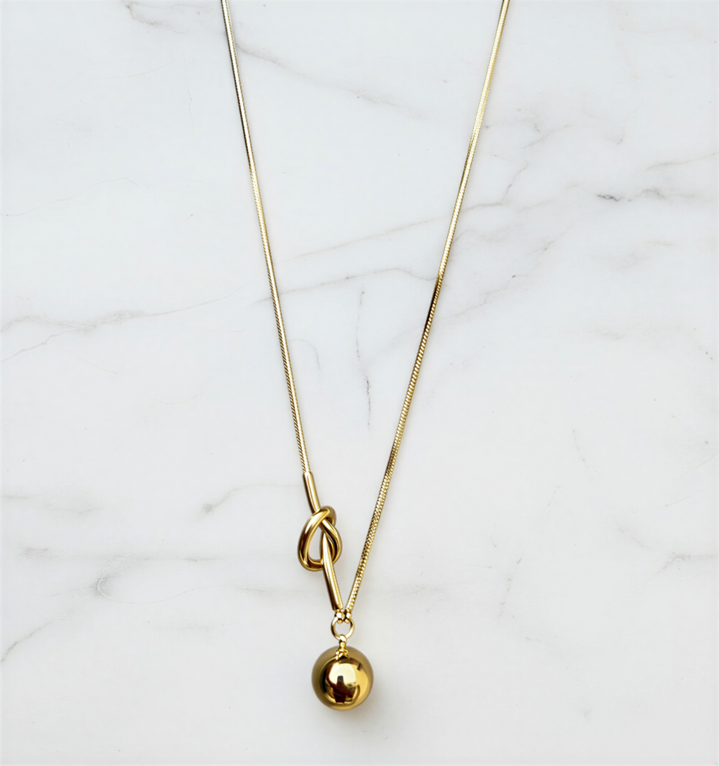 Gold necklace with a small gold ball pendant on a marble surface
