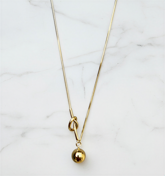 Gold necklace with a small gold ball pendant on a marble surface