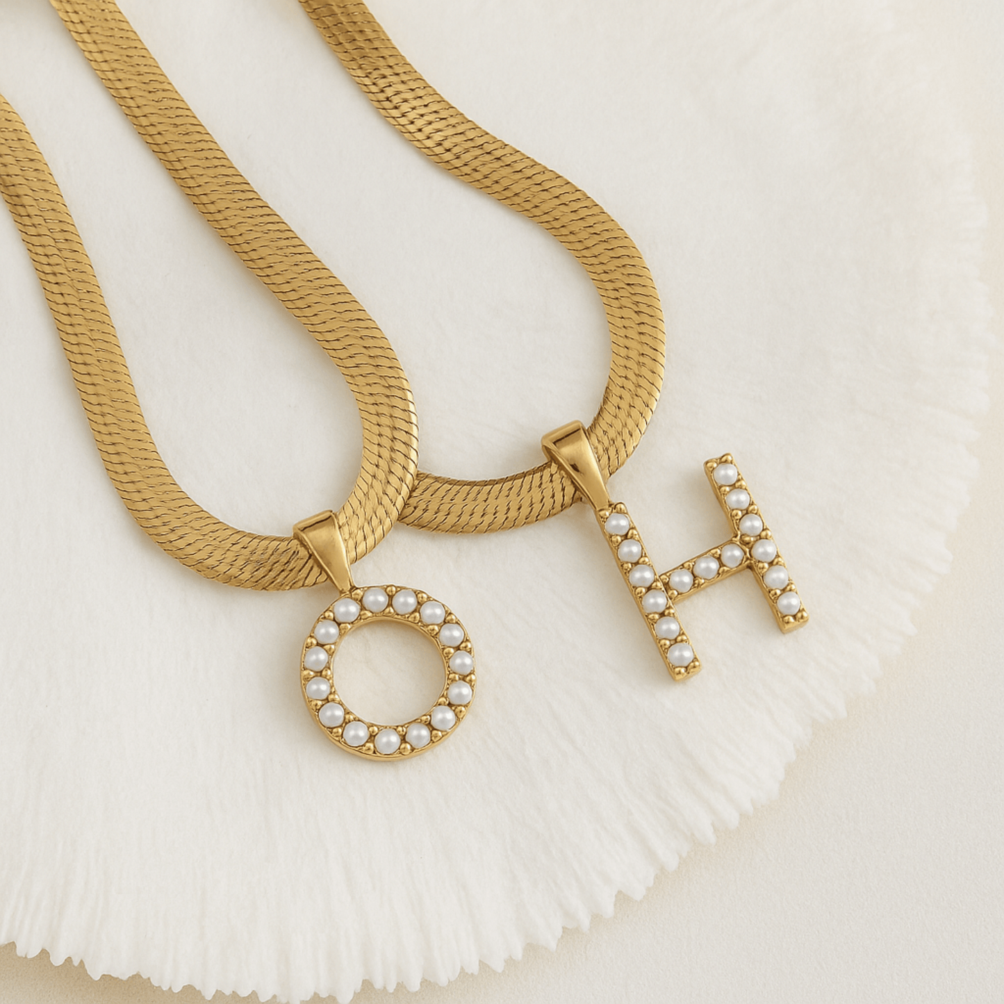 Gold necklaces with letter pendants on a textured white surface