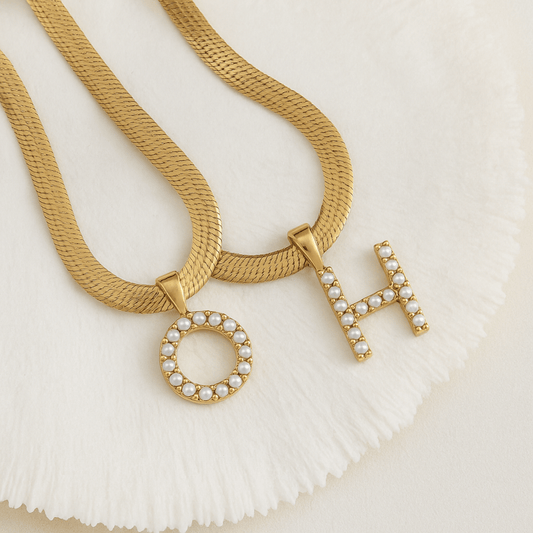 Gold necklaces with letter pendants on a textured white surface