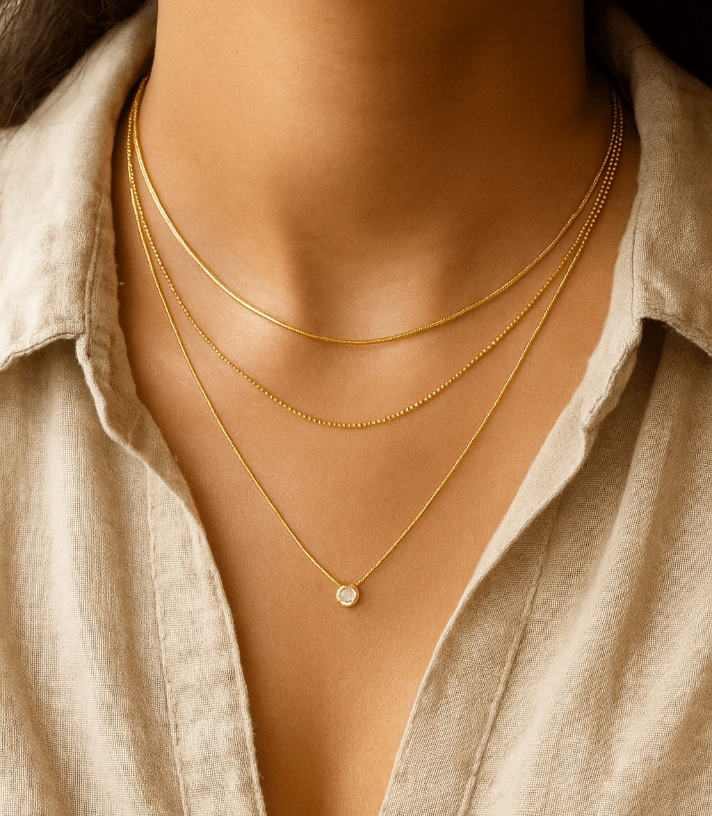 Close-up of a person wearing gold necklaces with a beige shirt.