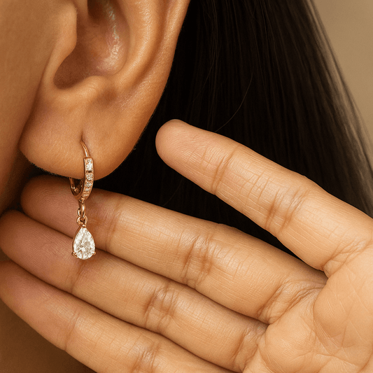 Gold earring with a teardrop-shaped gemstone worn by a person.