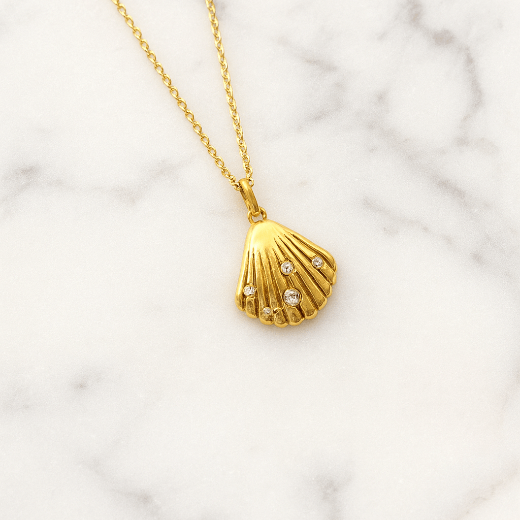Gold necklace with a shell pendant on a marble background