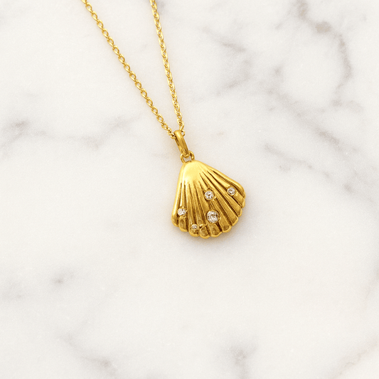 Gold necklace with a shell pendant on a marble background