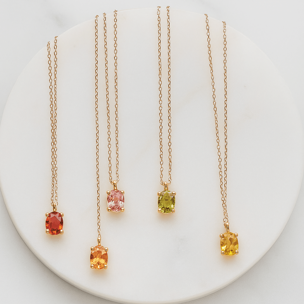Four gold necklaces with colored gemstones on a white plate