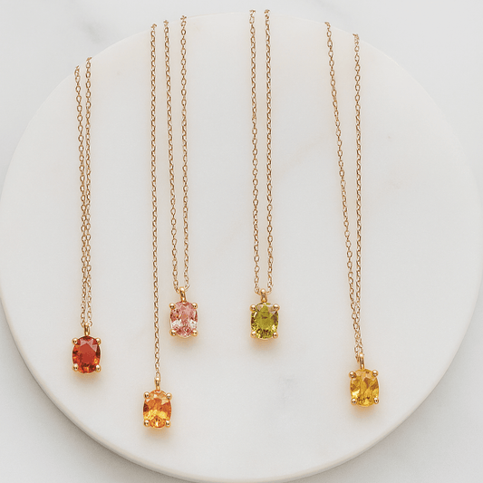 Four gold necklaces with colored gemstones on a white plate