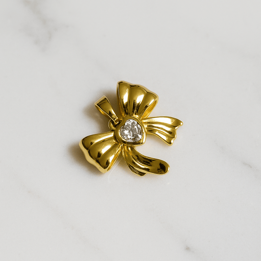 Gold bow-shaped brooch with a central gemstone on a marble background