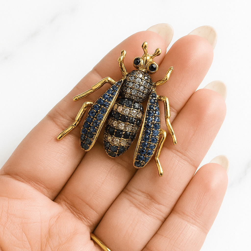 Gold and blue insect-shaped brooch on a hand against a white background