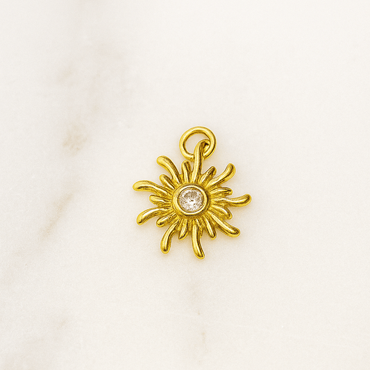 Gold sun-shaped pendant with a central gemstone on a white background