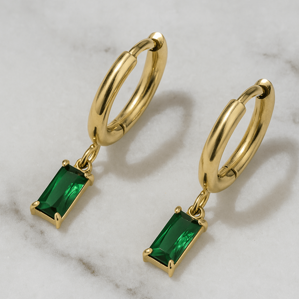 Gold hoop earrings with green gemstones on a marble background