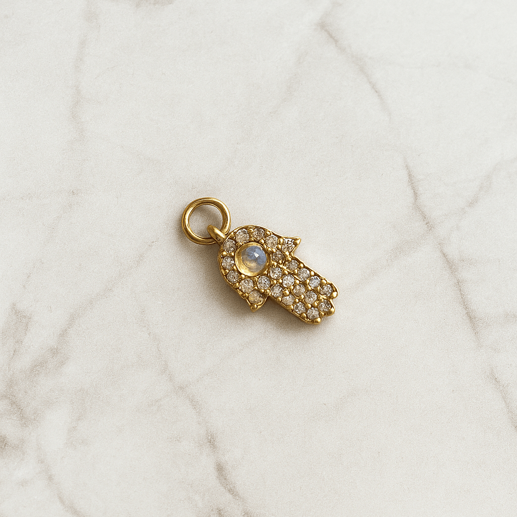 Gold hamsa hand charm with a gemstone on a marble surface