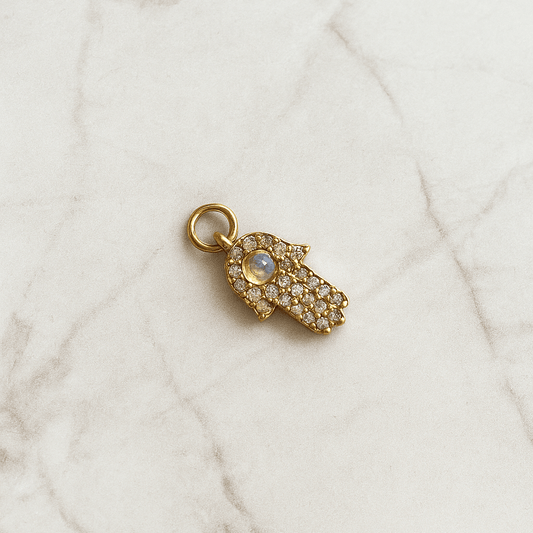 Gold hamsa hand charm with a gemstone on a marble surface