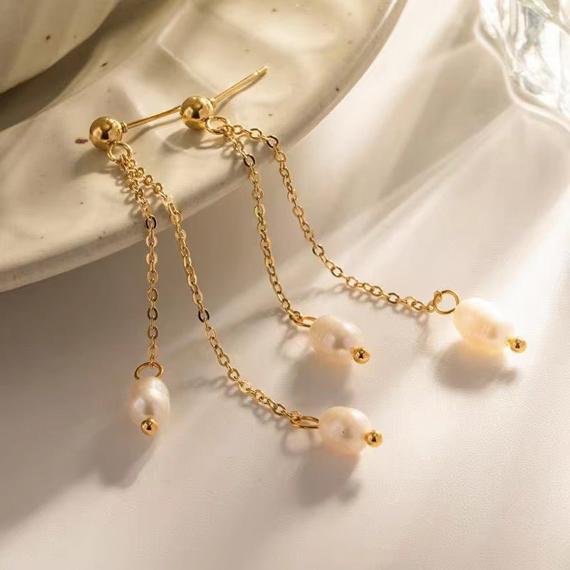 A pair of 18K gold bonded fresh water pearl earrings with golden chains, displayed against a creamy background.