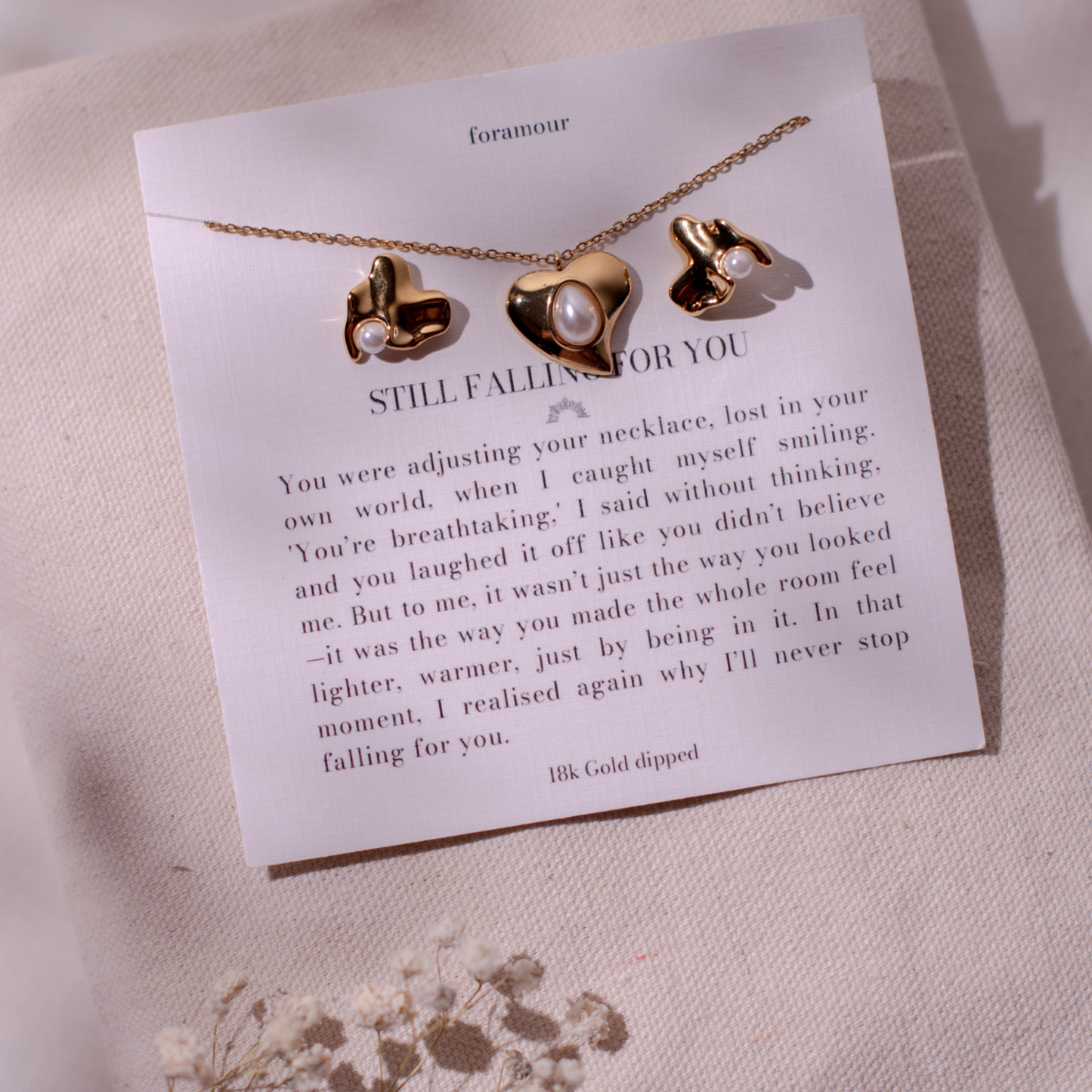 A gold-plated necklace with a heart-shaped pendant and a pair of earrings, presented on a card with a love-themed message.