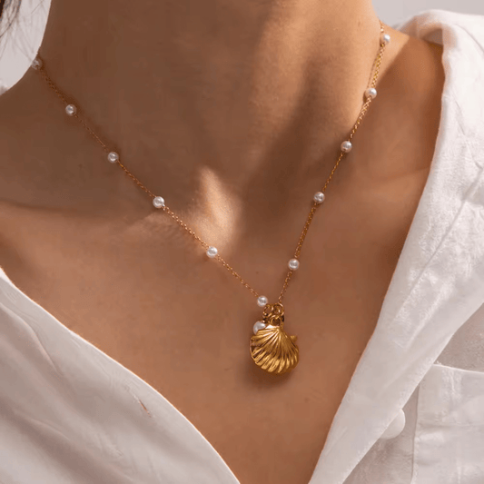 A person wearing a white shirt showcasing a gold necklace with a golden shell, starfish, and pearl charms.