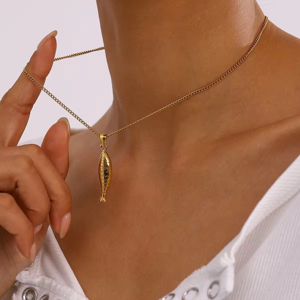 Gold necklace with a fish pendant worn by a person, against a neutral background