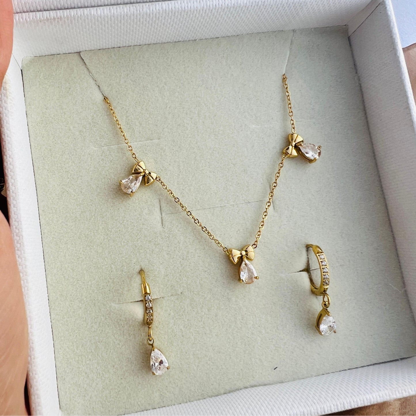 A gold pendant necklace with delicate bows and radiant teardrop stones, worn by a person.