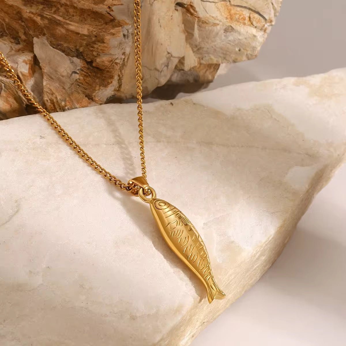 Gold fish-shaped pendant necklace on a stone surface