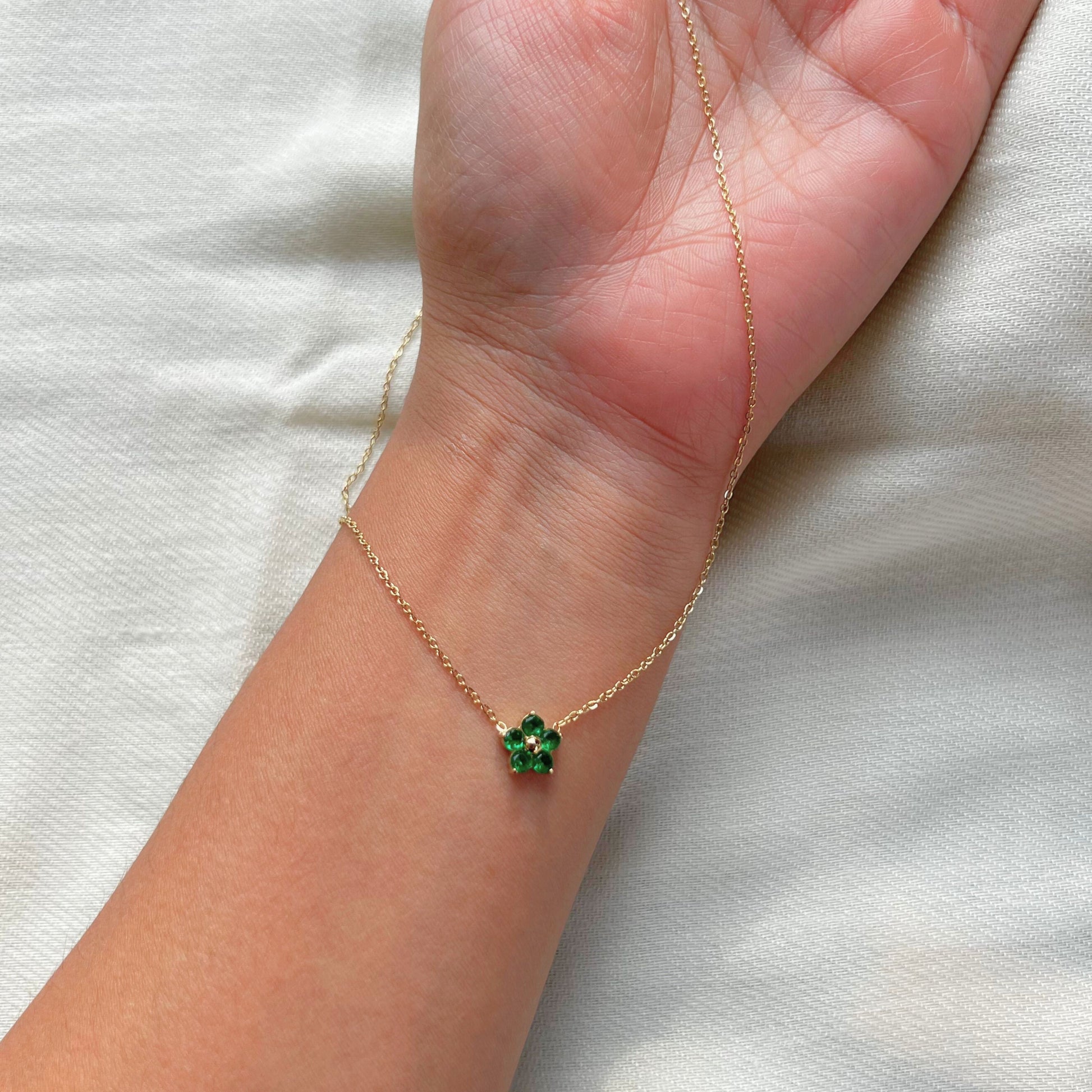 An 18k gold-dipped bee pendant necklace with a green emerald gemstone on a hand, showcasing the design and the length of the necklace.