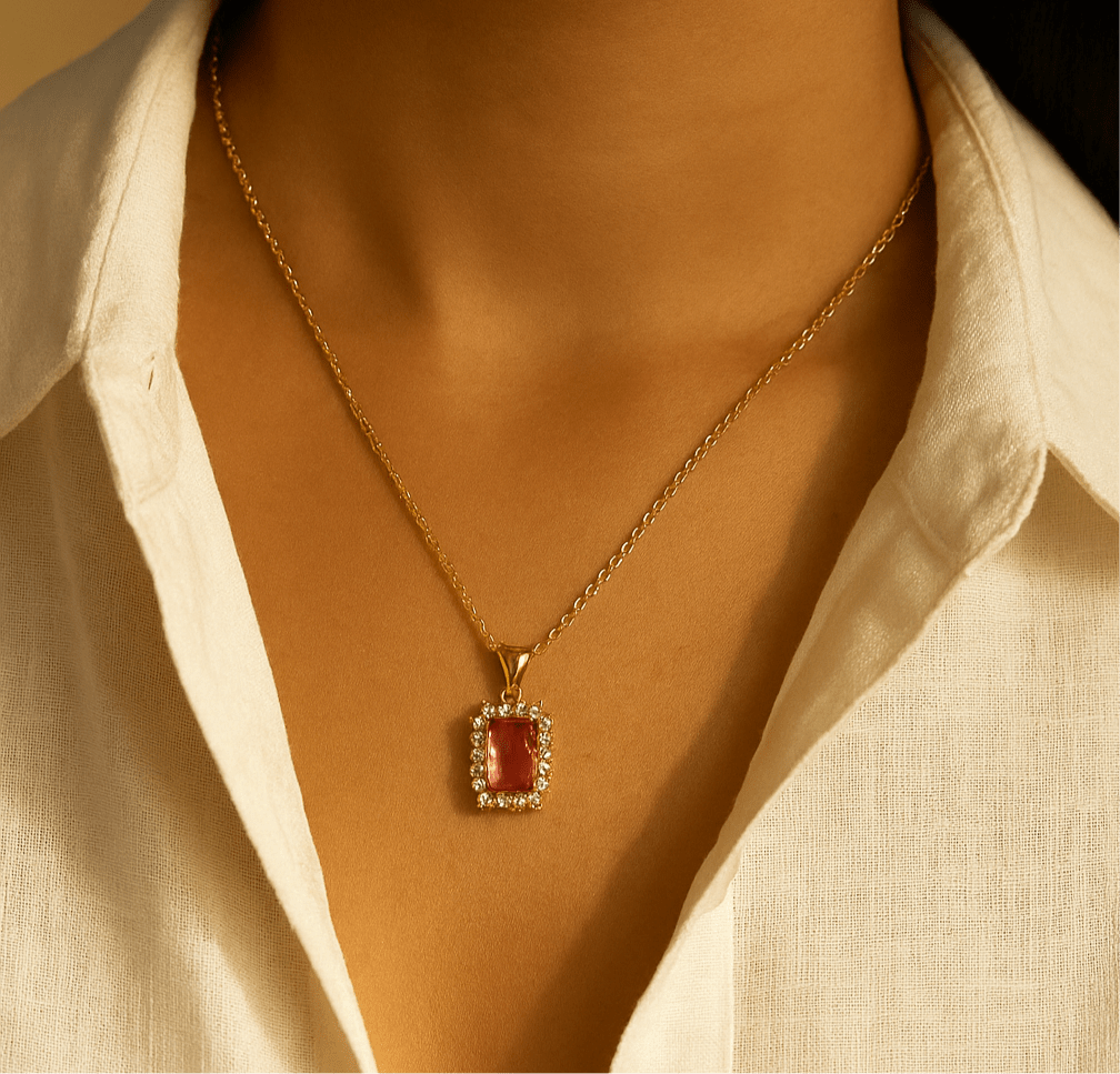Gold necklace with a red pendant worn by a person in a white shirt.