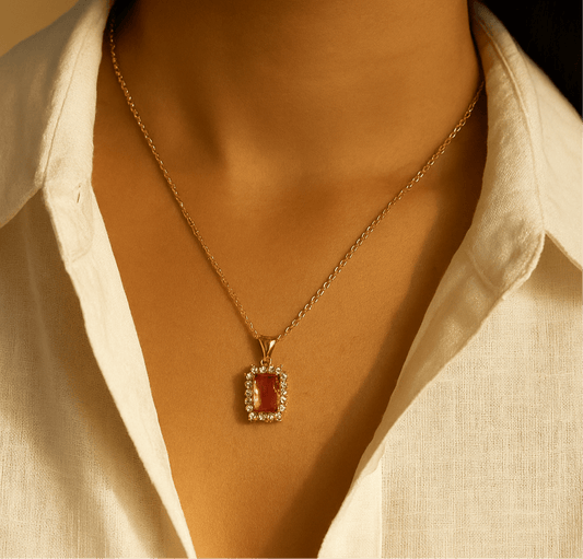 Gold necklace with a red pendant worn by a person in a white shirt.