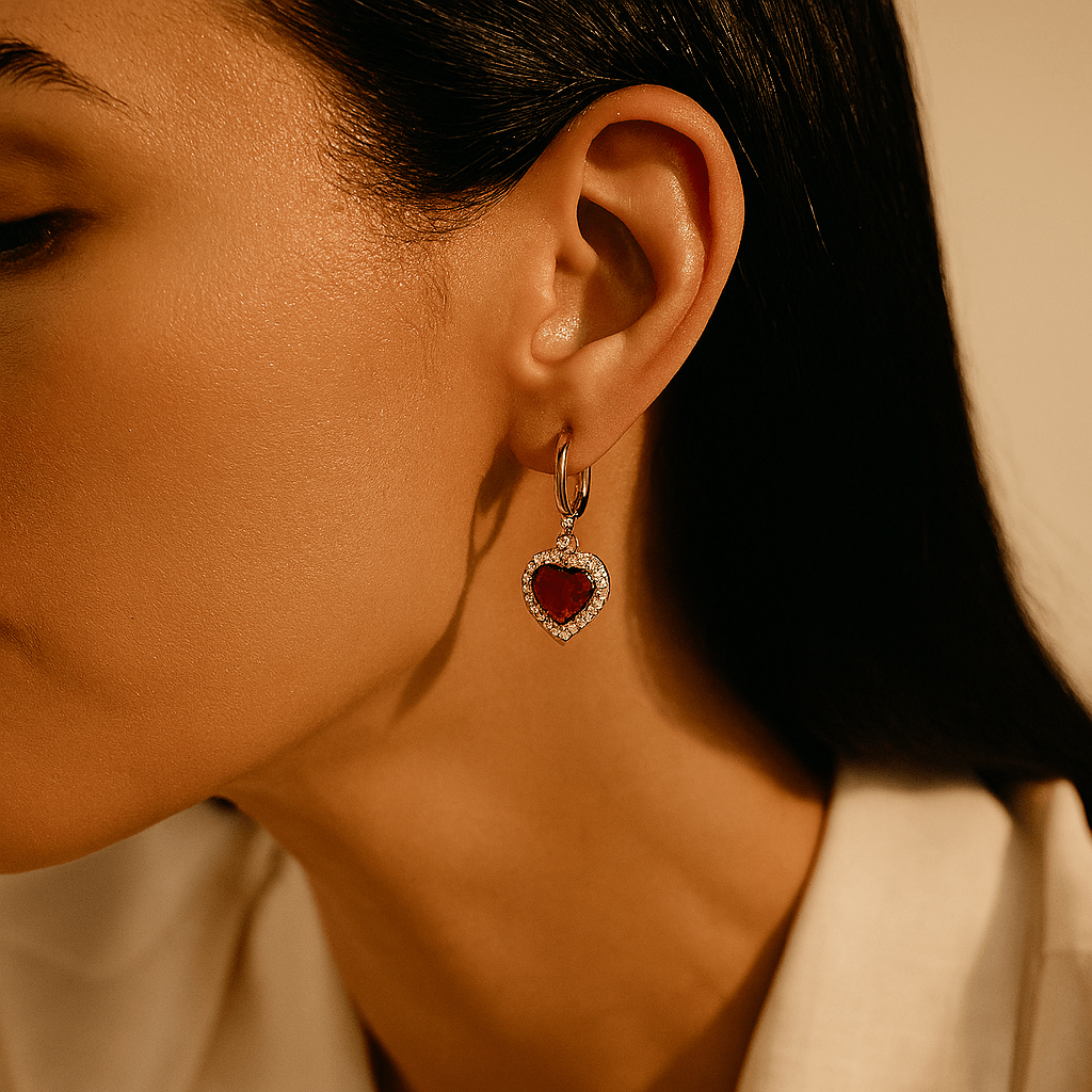 Close-up of a person wearing a heart-shaped earring with a red gemstone.