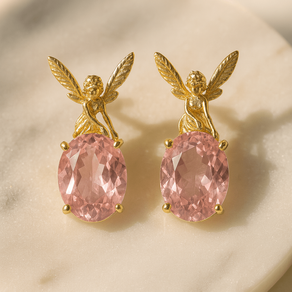 Gold angel earrings with pink gemstones on a beige background