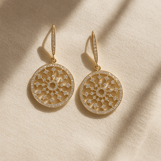 Gold earrings with intricate designs on a beige fabric background