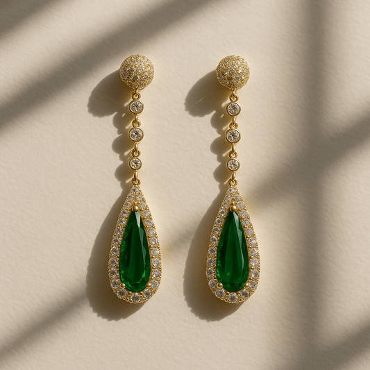 Gold earrings with green teardrop stones on a beige background