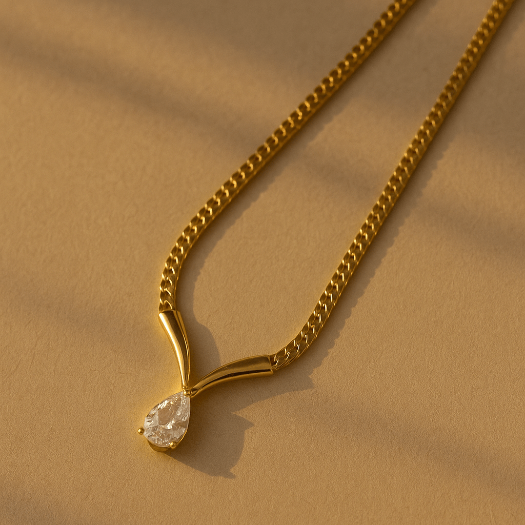 A gold-colored necklace with a single teardrop-shaped crystal pendant, displayed against a beige background.
