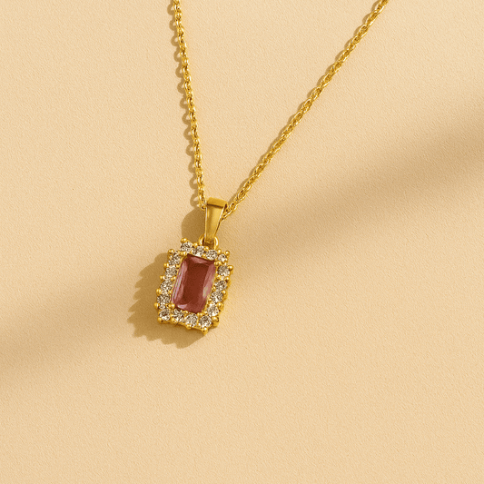 Gold necklace with a red gemstone pendant on a beige background
