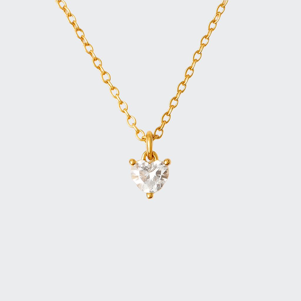 A gold-colored necklace with a heart-shaped pendant that is catching light, displayed against a white background.