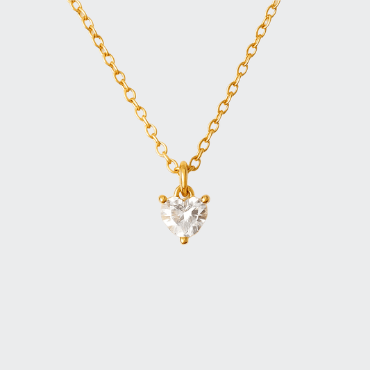 A gold-colored necklace with a heart-shaped pendant that is catching light, displayed against a white background.