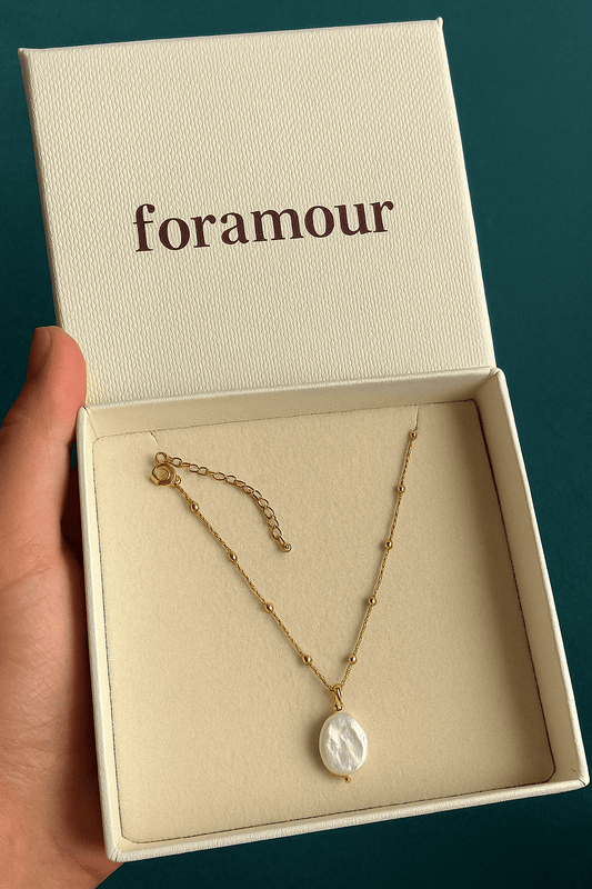 A gold chain necklace with a baroque pearl pendant, presented in a branded box with the text 'foramour'.