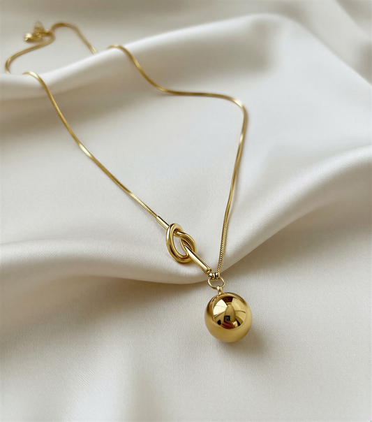 Gold necklace with a spherical pendant on a beige fabric background