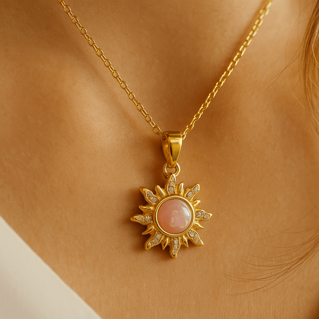 Gold necklace with a sun-shaped pendant featuring a pink stone on a person's neck.