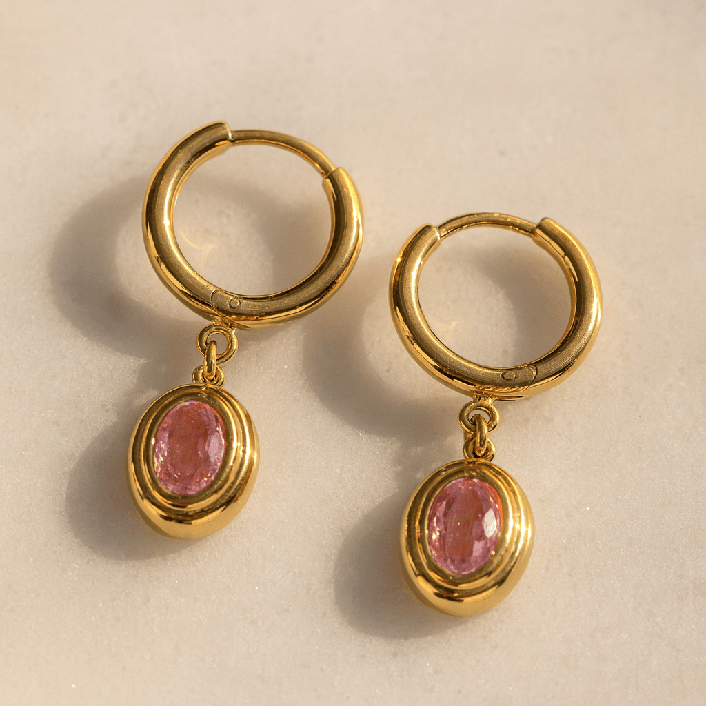 Gold hoop earrings with pink gemstones on a beige background