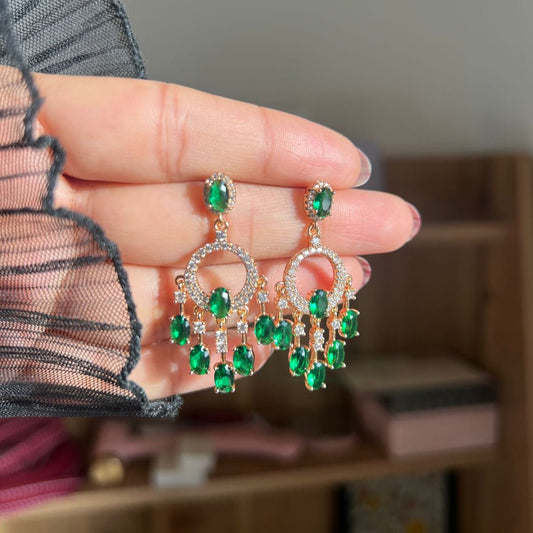 Green gemstone earrings held by a hand with a blurred background