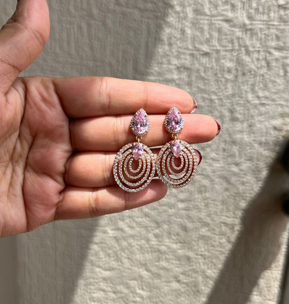 Hand holding a pair of ornate earrings against a neutral background