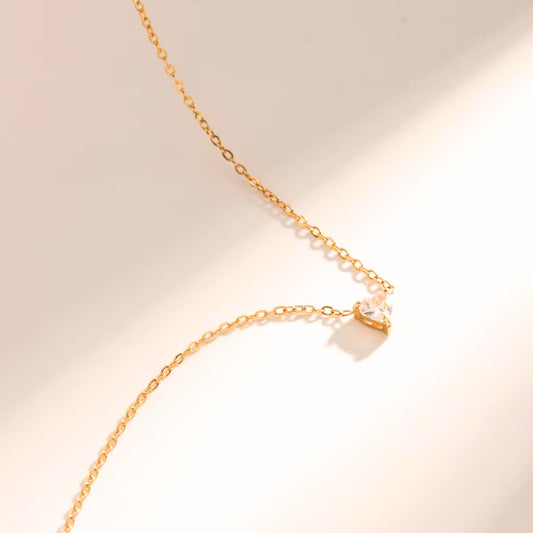 A delicate gold-tone heart-shaped necklace laid out on a plain surface, showcasing its elegant design and shiny finish.