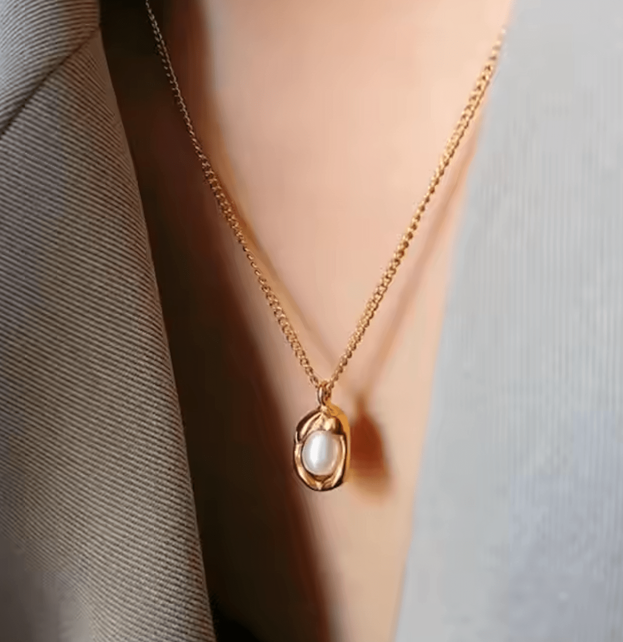 Gold necklace with a pearl pendant worn by a person against a neutral background