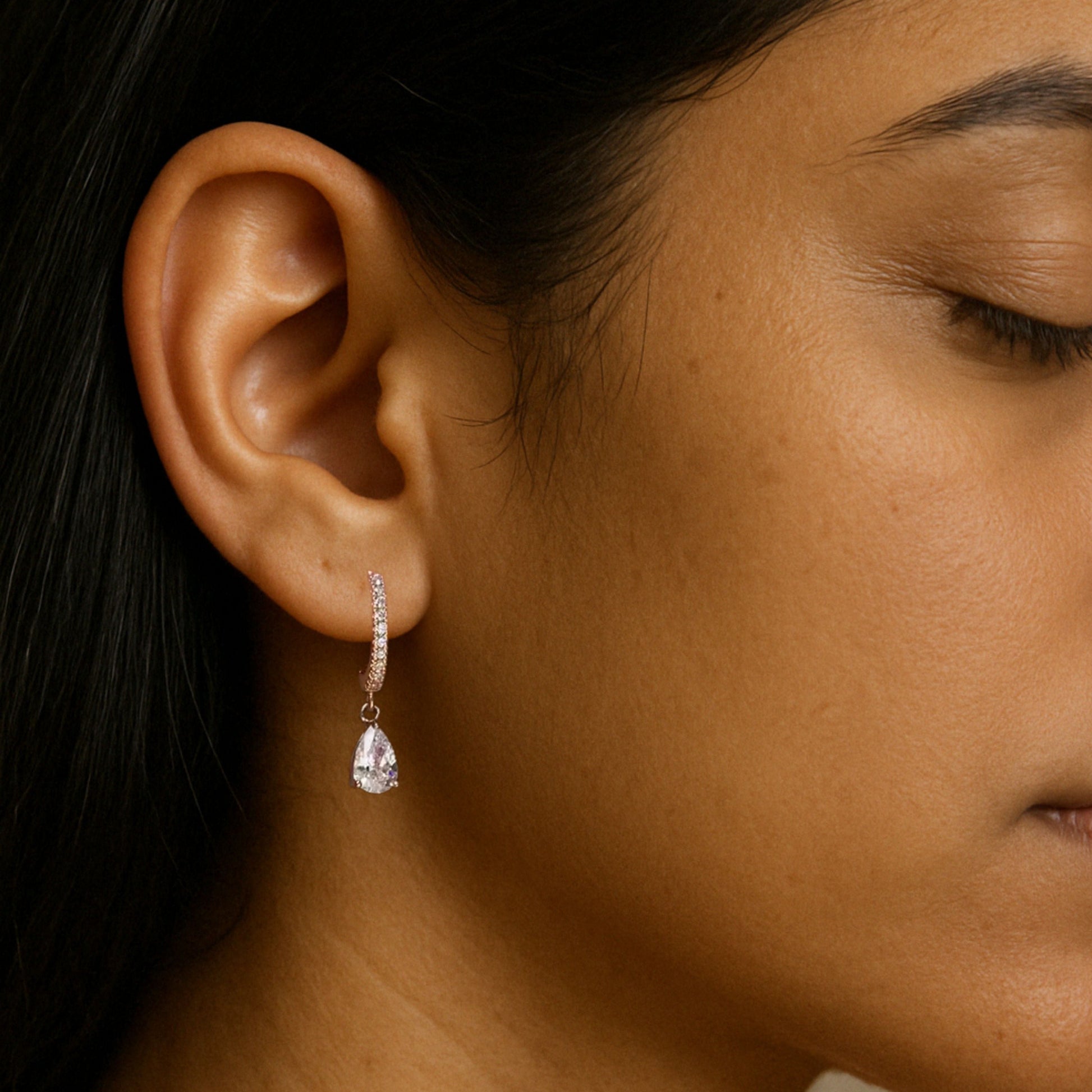 A close-up image of a woman's ear wearing a silver drop earring with a crystal accent.
