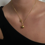 Gold necklace with a pendant on a person wearing a black top.