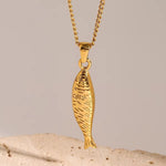Gold fish-shaped pendant on a chain against a beige background