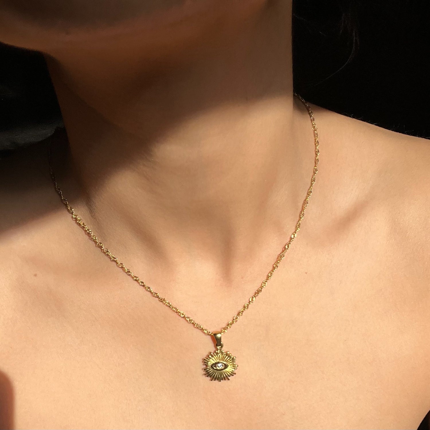 Gold necklace with a pendant on a person against a black background