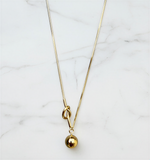 Gold necklace with a small gold ball pendant on a marble surface