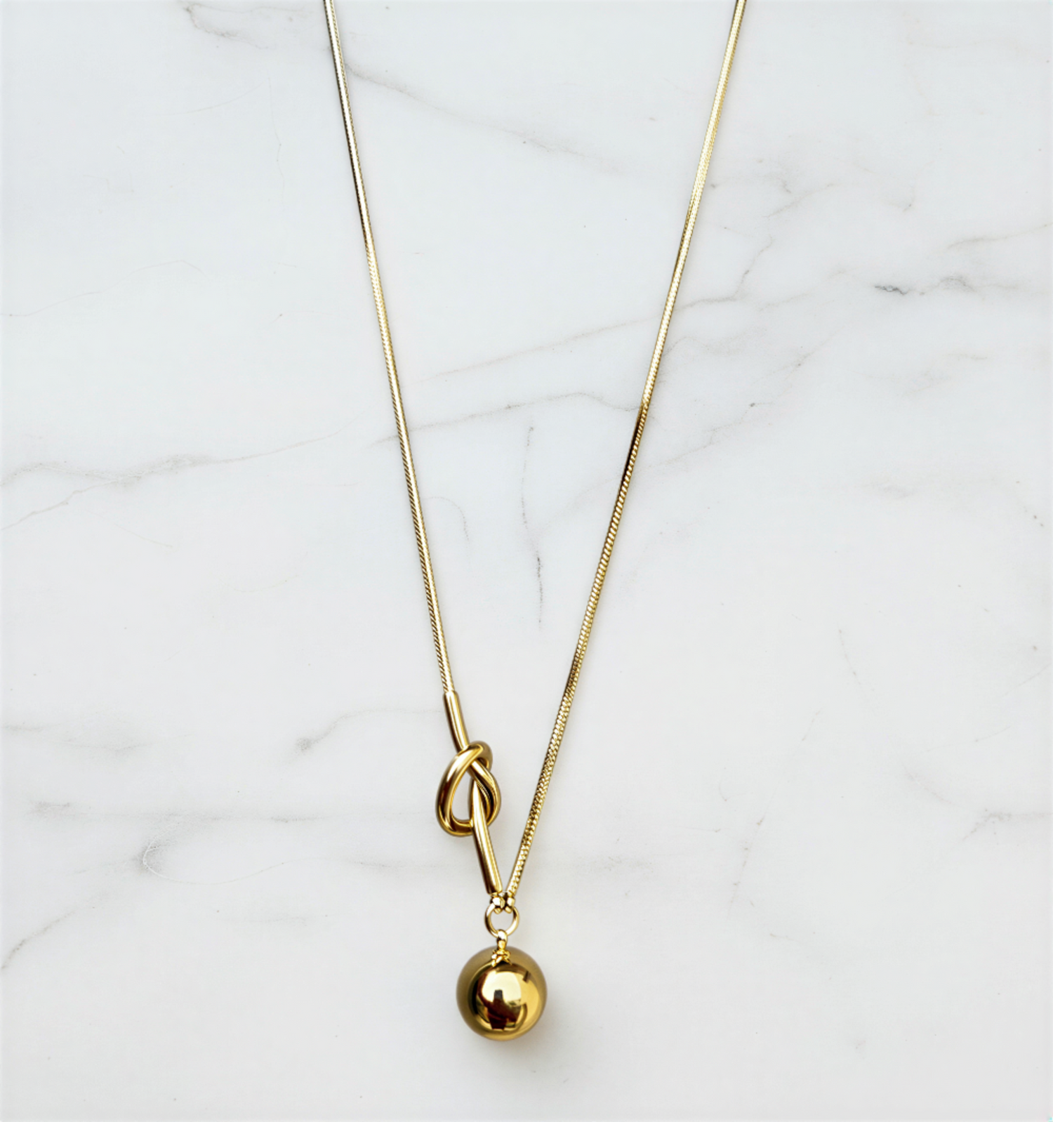 Gold necklace with a small gold ball pendant on a marble surface